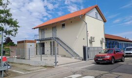 Weißes zweistöckiges Gebäude mit einem kleinen Fenster und vier Türen. Davor steht ein rotes Auto Weißes zweistöckiges Gebäude mit einem kleinen Fenster und vier Türen. Davor steht ein rotes Auto