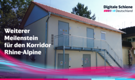 Zu sehen ist ein helles Gebäude mit vier Stahltüren und einer Stahltreppe an der Fassade, die in den ersten Stock führt. Davor steht: "Weiterer Meilenstein für den Korridor Rhine-Alpine" Zu sehen ist ein helles Gebäude mit vier Stahltüren und einer Stahltreppe an der Fassade, die in den ersten Stock führt. Davor steht: "Weiterer Meilenstein für den Korridor Rhine-Alpine"