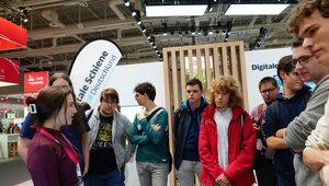 Mehrere Menschen stehen am Messestand der Digitalen Schiene Deutschland. Eine Frau spricht zu ihnen.