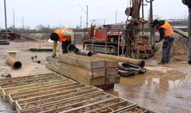 The picture shows the field of a rainy construction site with two men in orange high-visibility vests. (Copyright: DB InfraGO AG, Digitale Schiene Deutschland) The picture shows the field of a rainy construction site with two men in orange high-visibility vests. (Copyright: DB InfraGO AG, Digitale Schiene Deutschland)