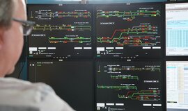 A man sits in front of a desk with four screens showing a field of tracks. A man sits in front of a desk with four screens showing a field of tracks.