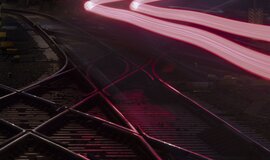 Two pairs of tracks crossing over two switch systems. Above them, two neon-colored lines created by long exposure of the rear lights of an ICE train. Two pairs of tracks crossing over two switch systems. Above them, two neon-colored lines created by long exposure of the rear lights of an ICE train.