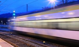 Das Foto zeigt zwei Gleise und einen Bahnsteig, an dem ein Zug vorbei rauscht.