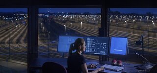 A person sitting on a desk with multible screens. In the background are multipble tracks. A person sitting on a desk with multible screens. In the background are multipble tracks.