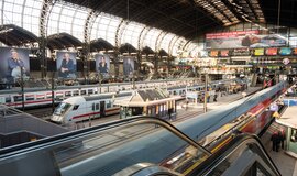Bahnhofshalle in Hamburg mit mehreren Zügen auf den Gleisen und Fahrgästen auf den Bahnsteigen.