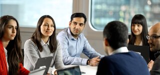 3 Personen an einem Tisch welche in einem Arbeitsmeeting sind.