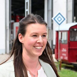 Portraitaufnahme von Anna Gunderlach: Eine lächelnde Frau mit langen braunen Haaren und einem hellgrünen Blazer