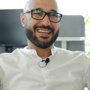 Das Portraitbild eines lächelnden Mannes mit Brille, Bart und weißem Hemd