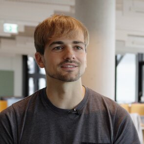 Das Portraitbild eines Mannes mit blonden Haaren, Dreitagebart und grauem T-Shirt