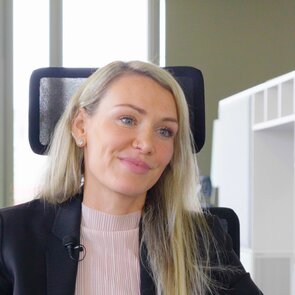 Portraitaufnahme einer Frau mit blonden Haaren, rosaner Bluse und schwarzem Jackett.