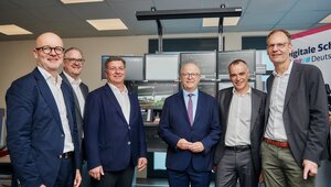 sechs Männer in Anzügen stehen vor einem modernen Bedienarbeitsplatz