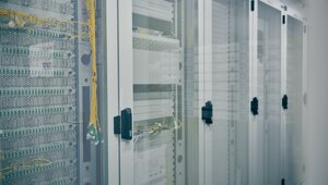 Five server cabinets with a glass front can be seen. Various compartments can be seen in the glass front, in each of which server modules are installed and connected with cables.