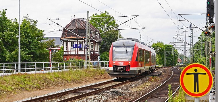 Roter Zug auf dem linken Gleis einer zweigleisigen Strecke mit Oberleitungen. Links der Bahnstrecke befindet sich ein altes Fachwerkhäuschen. Roter Zug auf dem linken Gleis einer zweigleisigen Strecke mit Oberleitungen. Links der Bahnstrecke befindet sich ein altes Fachwerkhäuschen.