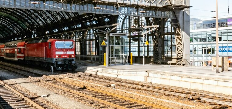Eine rote Lok steht unter den Stahlträgern am Dresdner Hauptbahnhof neben einem Bahnsteig.