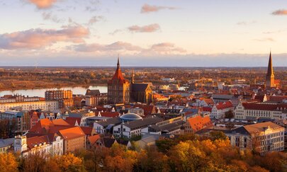 Titelbild Lückenschluss Rostock Seehafen – Kavelstorf Das Titelbild zeigt den Blick auf die Rostocker Altstadt im Vordergrund der Warnow