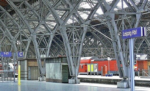 Trainstation with steelconstruction. Red Train standing at platform. Sign at platforms says "Leipzig HBF"
