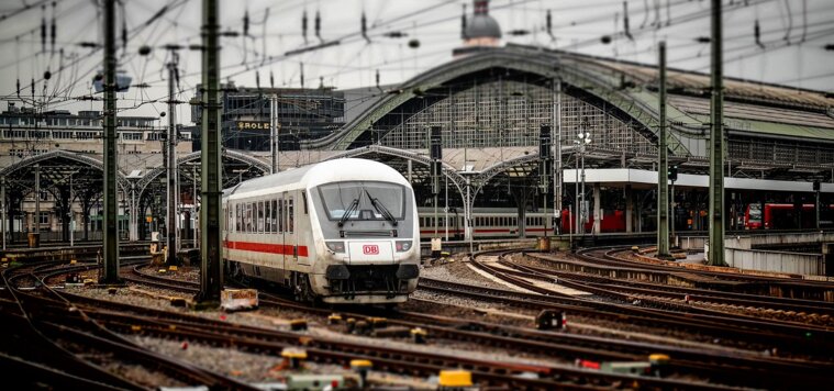 Ein weißer Zug fährt aus einem Bahnhof mit Stahlträgerdach Ein weißer Zug fährt aus einem Bahnhof mit Stahlträgerdach