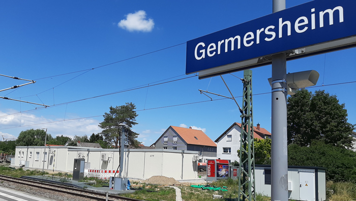 Sicht vom Bahnsteig auf ein flaches Gebäude im Hintergrund. Das blaue Schild auf dem Bahnsteigt schreibt "Germersheim".