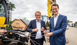 Zwei Menschen (links Ronald Pofalla, rechts Hendrik Wüst) stehen auf einer Baustelle und halten Kabel.